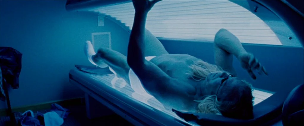 The Wrestler (2008) movie still: medium — A man lies inside a tanning bed with the lid partially closed. He wears dark glasses and a towel while his…
