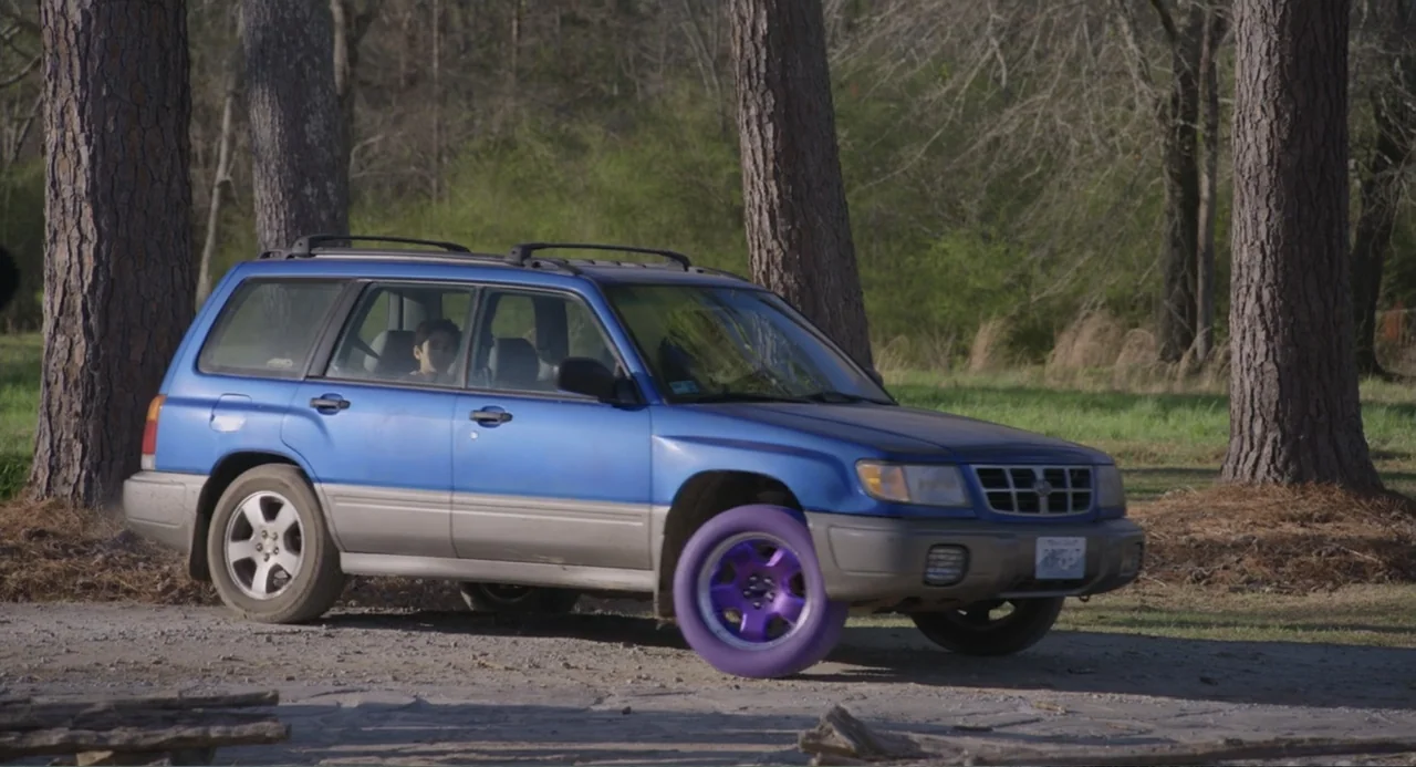Harold and the Purple Crayon (2024) movie still: medium — A blue station wagon with a bright purple front wheel is parked on a dirt path. A teenage…