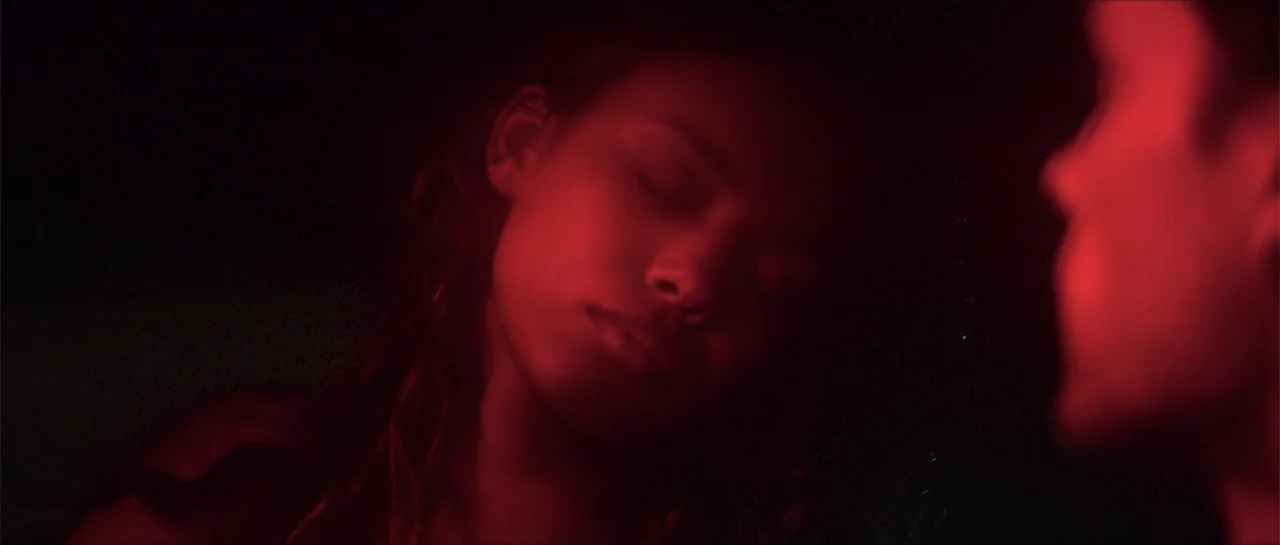 68 Kill (2017) movie still: closeup — The interior of a vehicle at night is bathed in deep red light. A young woman with dark hair rests her eyes…
