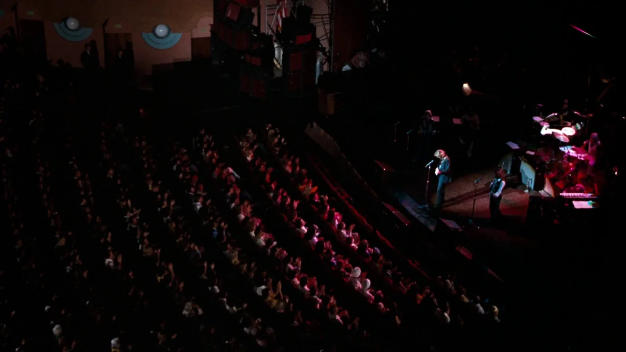 A Star Is Born (1976) movie still: wide — An expansive concert hall features a dark auditorium filled with a seated audience. Two musicians stand on…