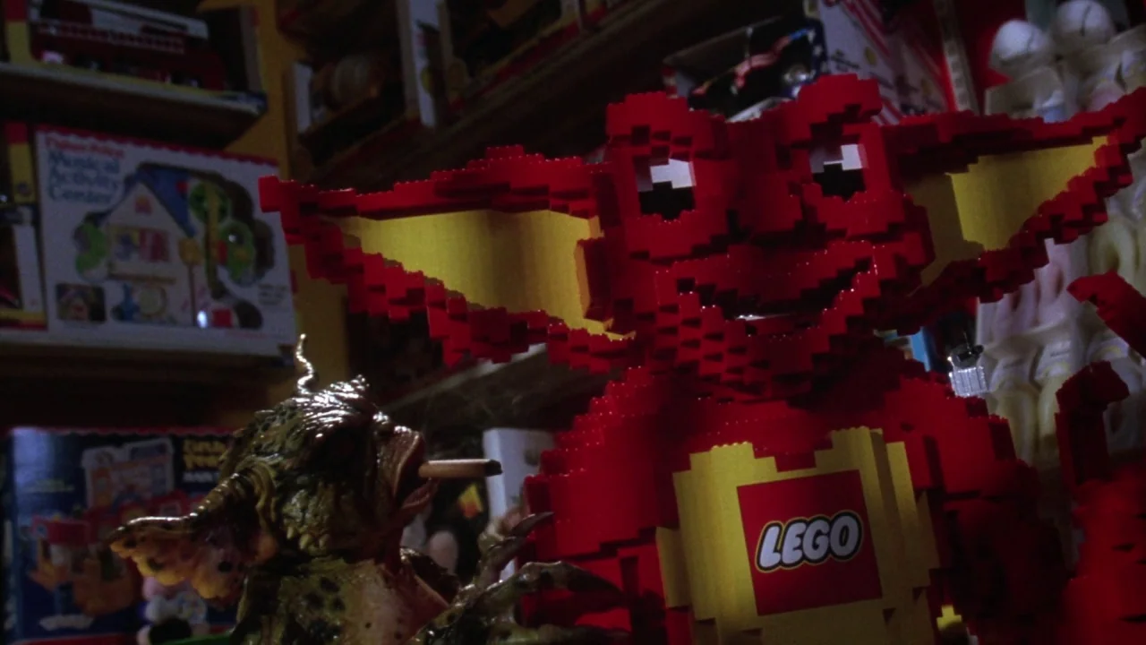 Gremlins 2: The New Batch movie still: medium — A dimly lit toy store aisle features rows of boxed children's products on shelves. A large red…
