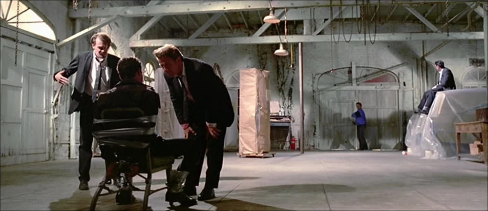 Reservoir Dogs (1992) movie still: wide — A spacious, sterile room with white-painted brick walls and high exposed timber rafters. Three men in…