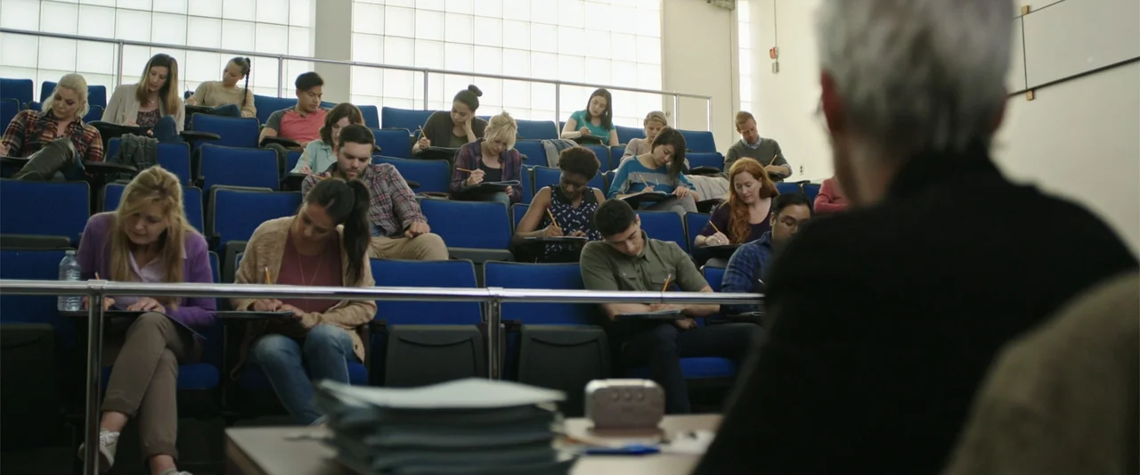 Overboard (2018) movie still: medium — A modern university lecture hall features tiered blue seating arranged in rows facing forward. Numerous…