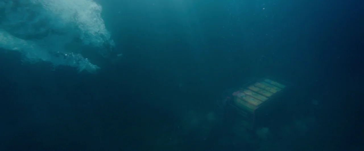 Paddington 2 (2017) movie still: wide — An underwater scene features a vast expanse of dark blue water and light rays. A rectangular metal box…