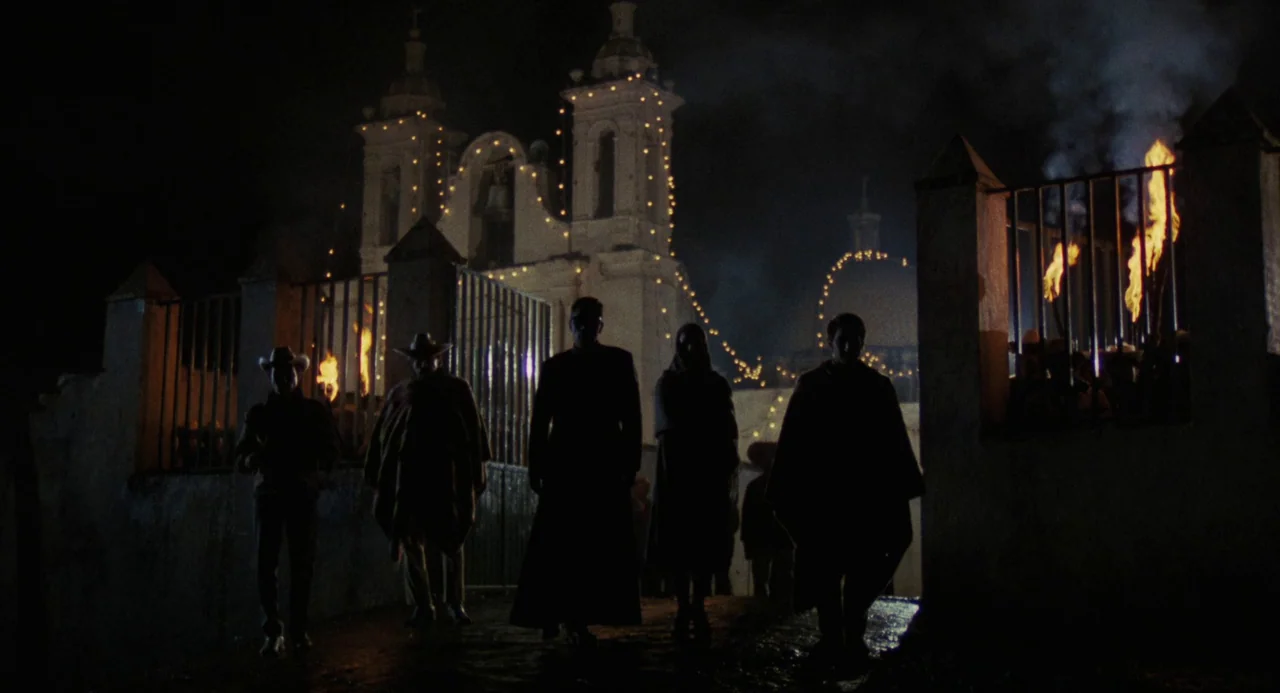 Canoa: A Shameful Memory (1976) movie still: fullbody — A group of five figures walks toward the camera across a cobblestone square. A large…