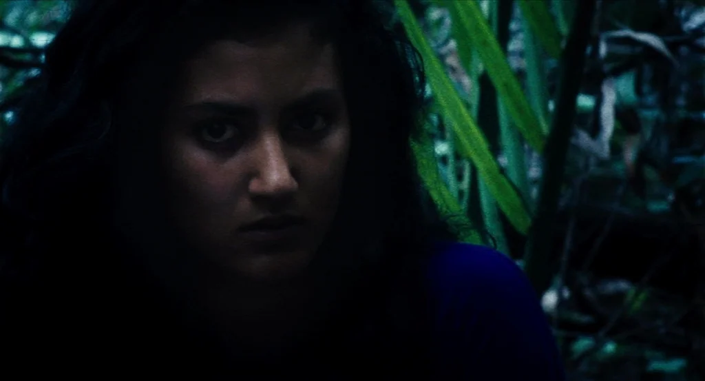 Almayer’s Folly (2011) movie still: closeup — A dark, dense tropical forest environment at night with thick vegetation and large leaves. A young…