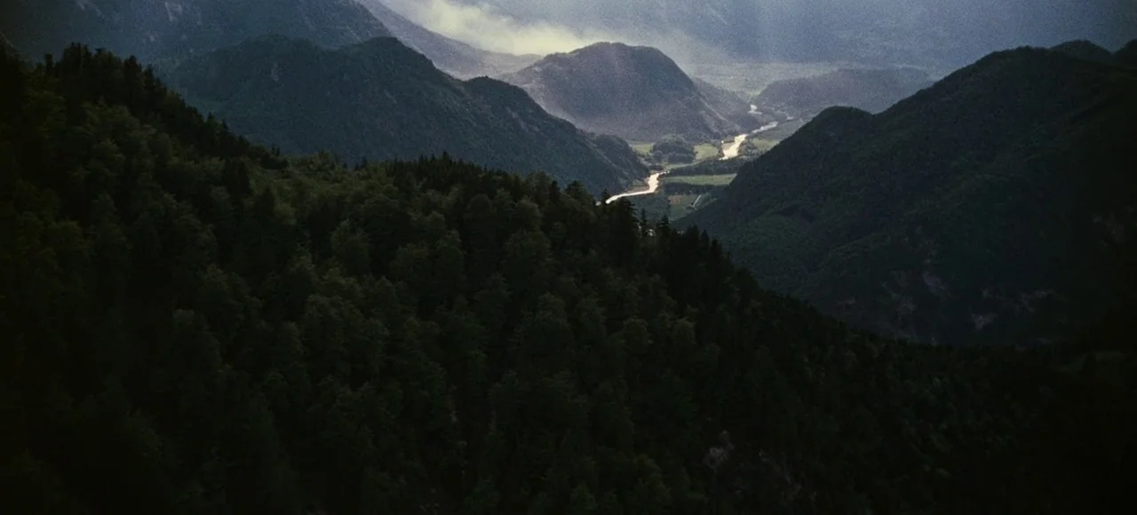 The Sound of Music (1965) movie still: establishing — A dense forest covers the foreground mountain slopes overlooking a deep alpine valley. A…