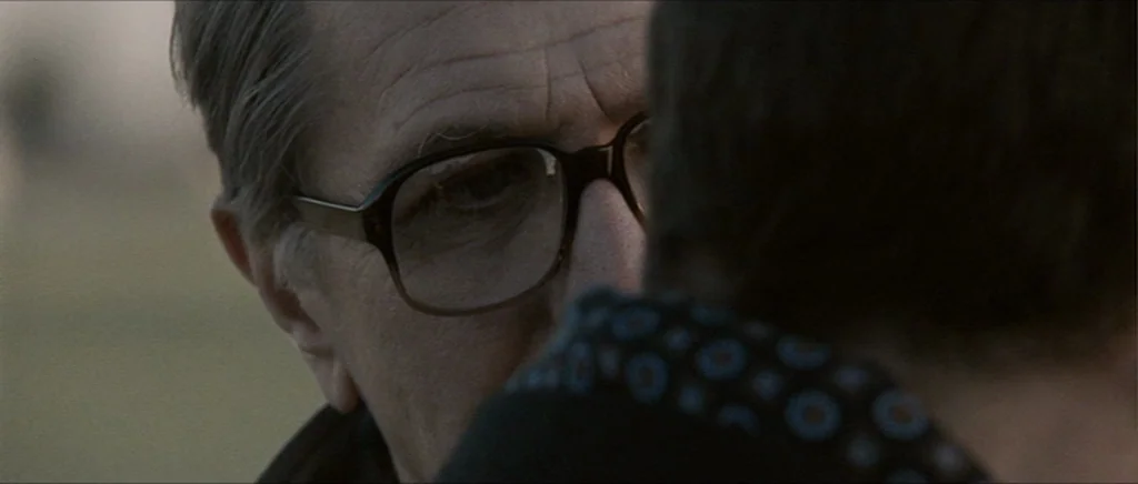Tinker Tailor Soldier Spy (2011) movie still: closeup — An older man wearing glasses stares at a person whose back is to camera. They stand in an…