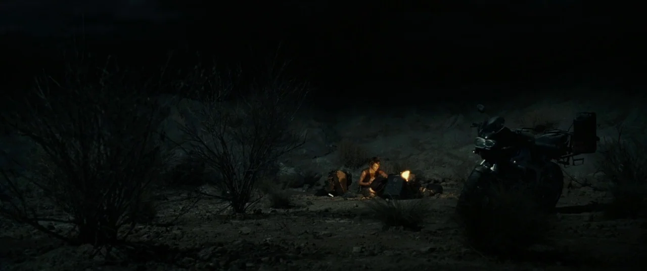 Resident Evil: Extinction (2007) movie still: wide — A dark, rocky desert landscape at night with sparse dry vegetation and rolling terrain. A lone…