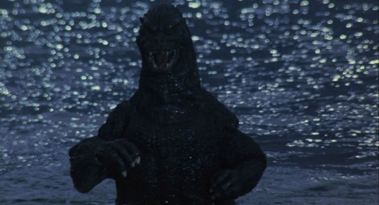 Godzilla vs. Mechagodzilla II (1993) movie still: medium — A dark, textured reptilian creature emerges from a deep blue body of water at night. The…