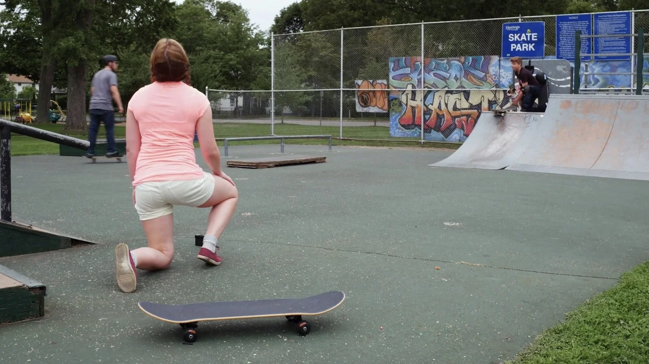 Sk8 Dawg (2018) movie still: medium — An outdoor skate park features a metal ramp with graffiti and a chain-link fence. A woman in a pink shirt…