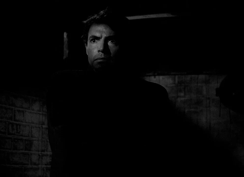 Odd Man Out (1947) movie still: medium — A dark space features a textured brick wall visible on the left side. A man in a dark suit occupies the…