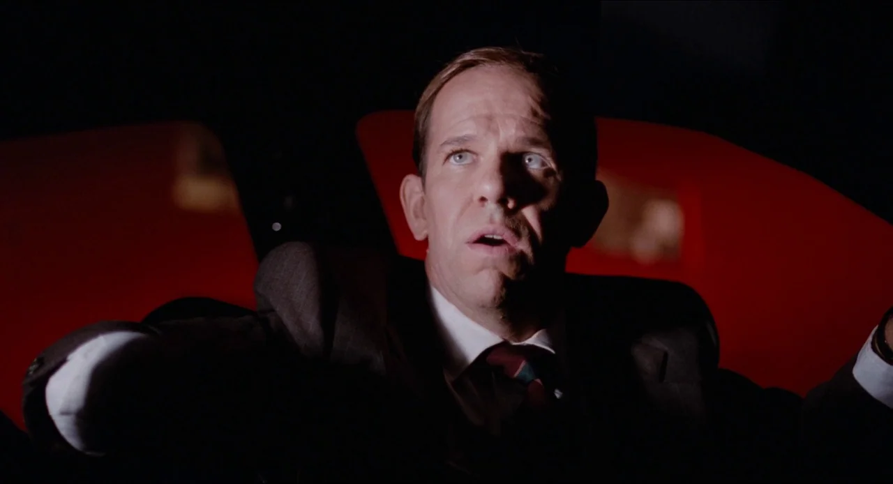 Deep Cover (1992) movie still: closeup — The interior of a vehicle is cast in deep darkness with bright red ambient light. A man in a suit sits…