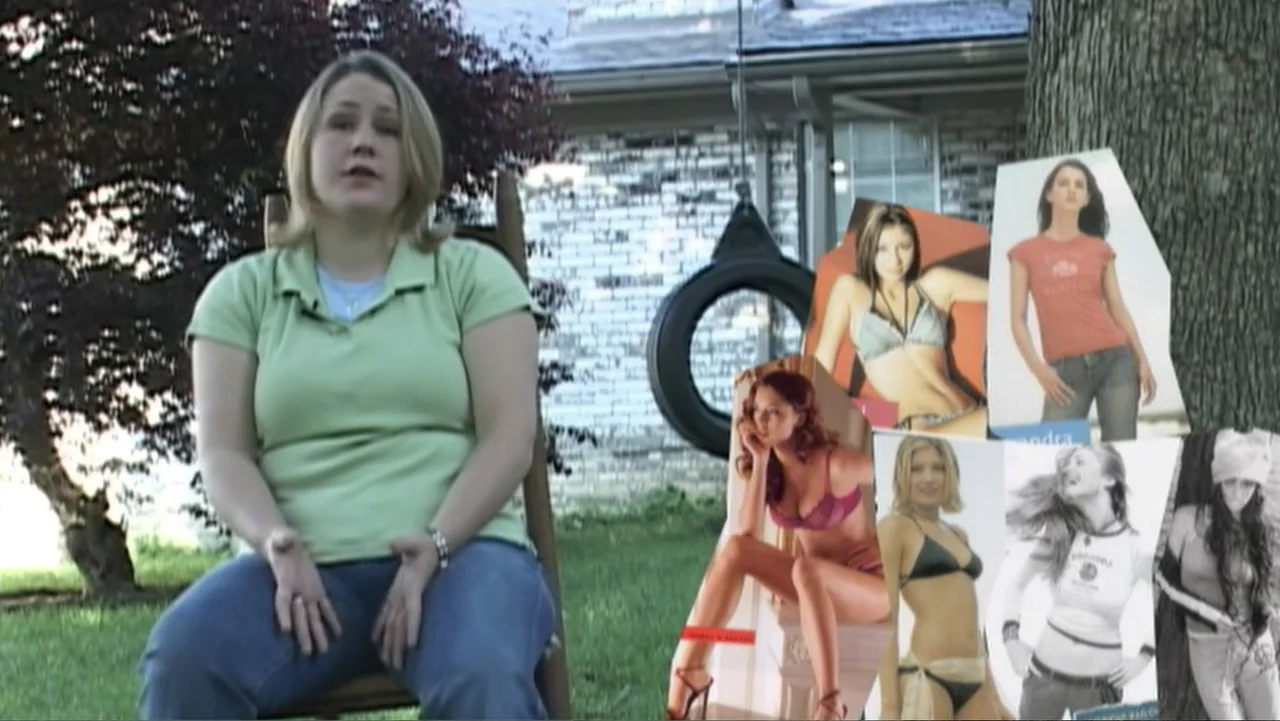 Super Size Me (2004) movie still: medium — A woman sits in a wooden rocking chair in a green residential backyard. Several large cardboard cutouts…
