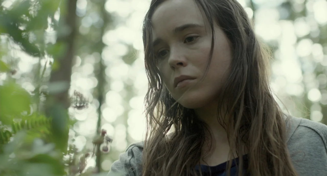 En lo profundo del bosque movie still: closeup — A woman stands in a dense, out-of-focus forest setting with overgrown vegetation. She gazes…