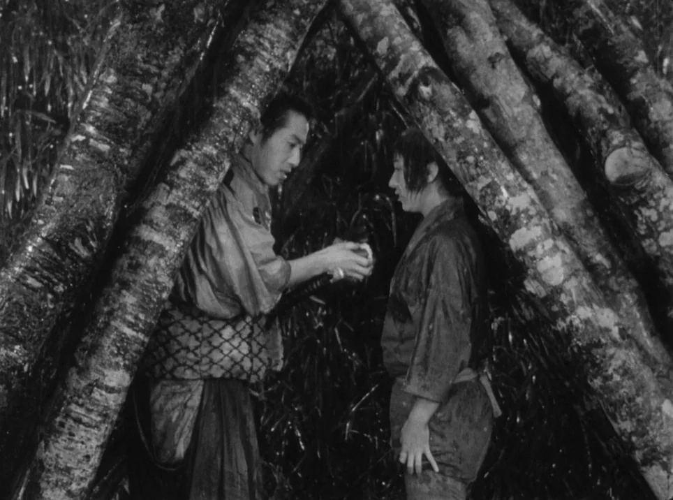 Seven Samurai (1954) movie still: medium — A crude lean-to shelter constructed from thick, rough-hewn tree trunks and branches. One man stands and…