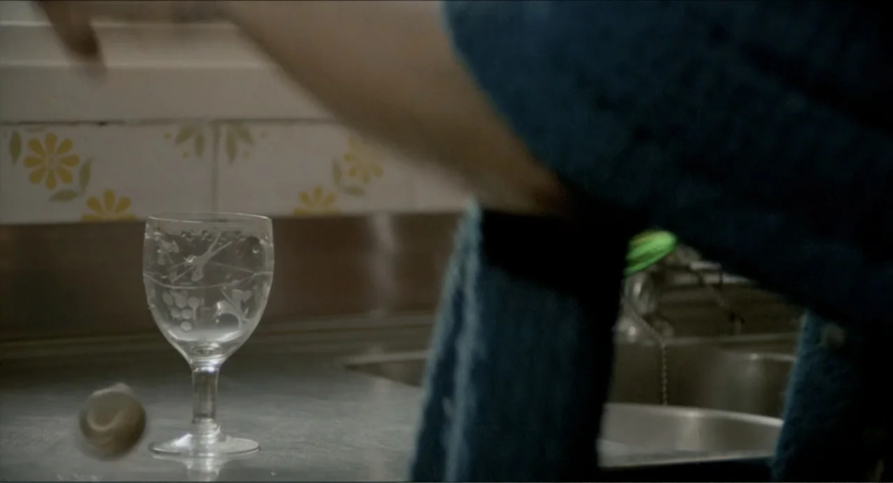 Waiting for the Hearse (1985) movie still: closeup — A kitchen counter features floral-patterned tiles on the wall behind a metal sink. An empty…