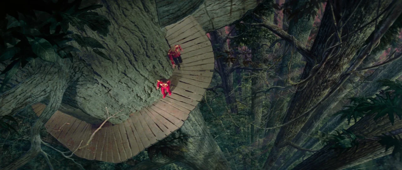 Flash Gordon (1980) movie still: wide — A wooden circular bridge winds around the massive trunk of a giant ancient tree. Two figures in matching red…