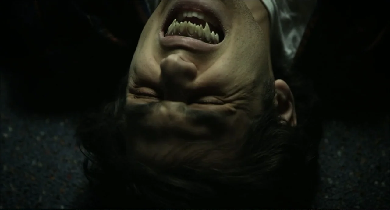 Freedom (2024) movie still: closeup — The frame shows a face from a low angle on a textured carpet. A man lies on his back with his mouth open to…