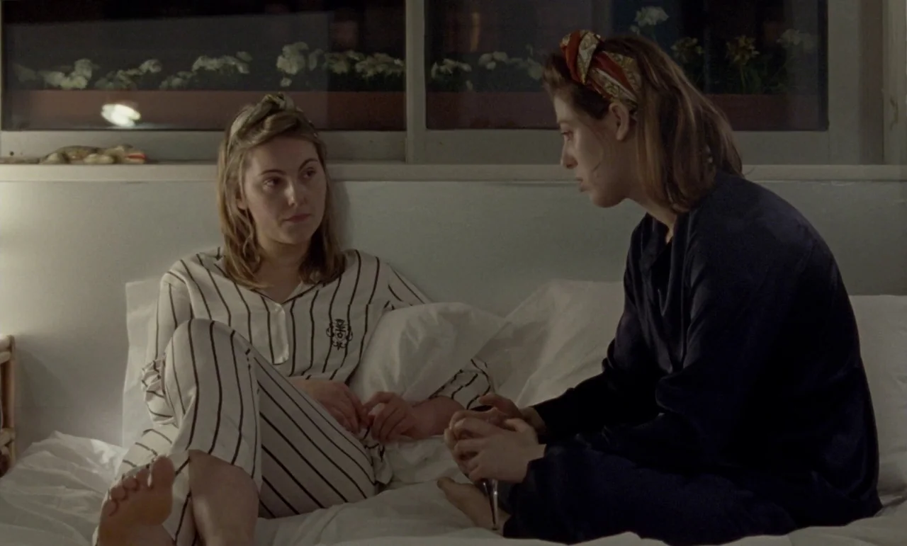 The Souvenir: Part II (2021) movie still: medium — Two women sit on a bed in a minimally decorated room at night. They face each other while having…