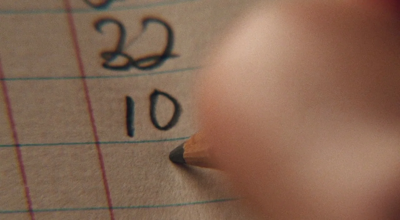 Phantom Thread (2017) movie still: closeup — A sheet of off-white lined paper features handwritten numbers written in black ink. A pencil tip is…