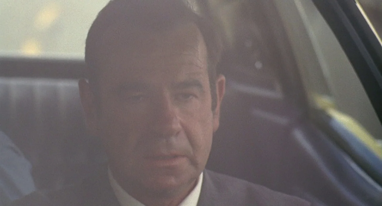 Charley Varrick (1973) movie still: closeup — A man sits inside the interior of a 1970s vehicle during daylight hours. The man faces slightly away…