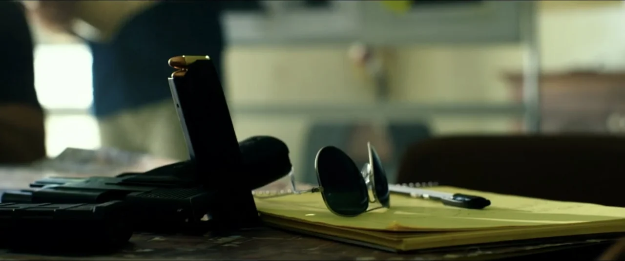 13 Hours: The Secret Soldiers of Benghazi (2016) movie still: closeup — A wooden table contains a yellow notepad, sunglasses, a handgun, and a…