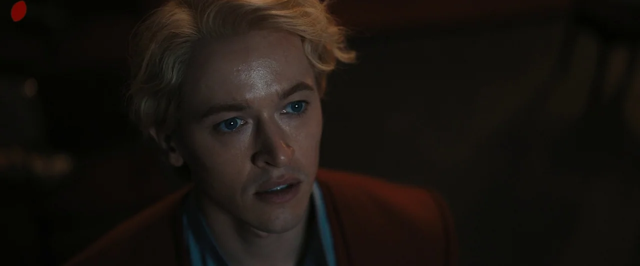 The Hunger Games: The Ballad of Songbirds & Snakes (2023) movie still: closeup — A man with blonde hair sits in a dark, indistinct interior setting.…
