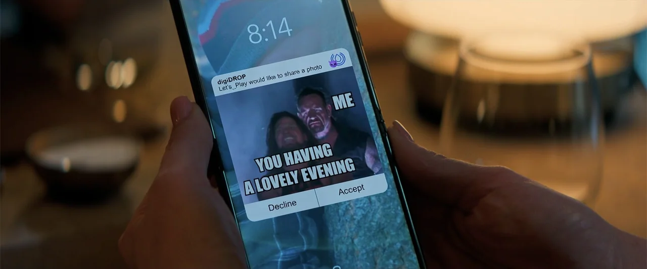 Drop (2025) movie still: closeup — A modern smartphone screen displays a digital notification overlaying a meme image. Hands hold the device against…