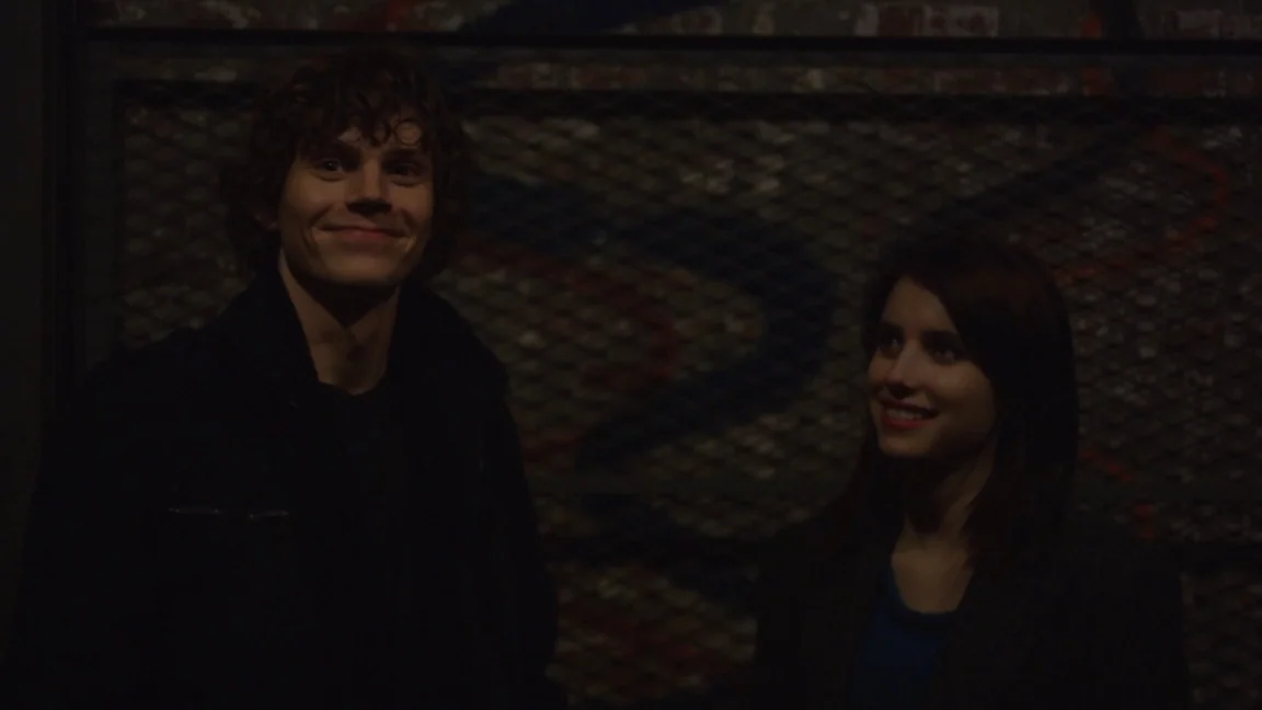 Adult World (2013) movie still: medium — A man and woman stand in a dark, dim industrial space with metal grid walls. Both individuals are looking…