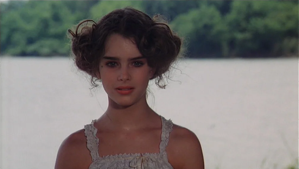 Pretty Baby (1978) movie still: medium — A teenage girl stands outdoors with a river and green forest in the background. She faces the camera…