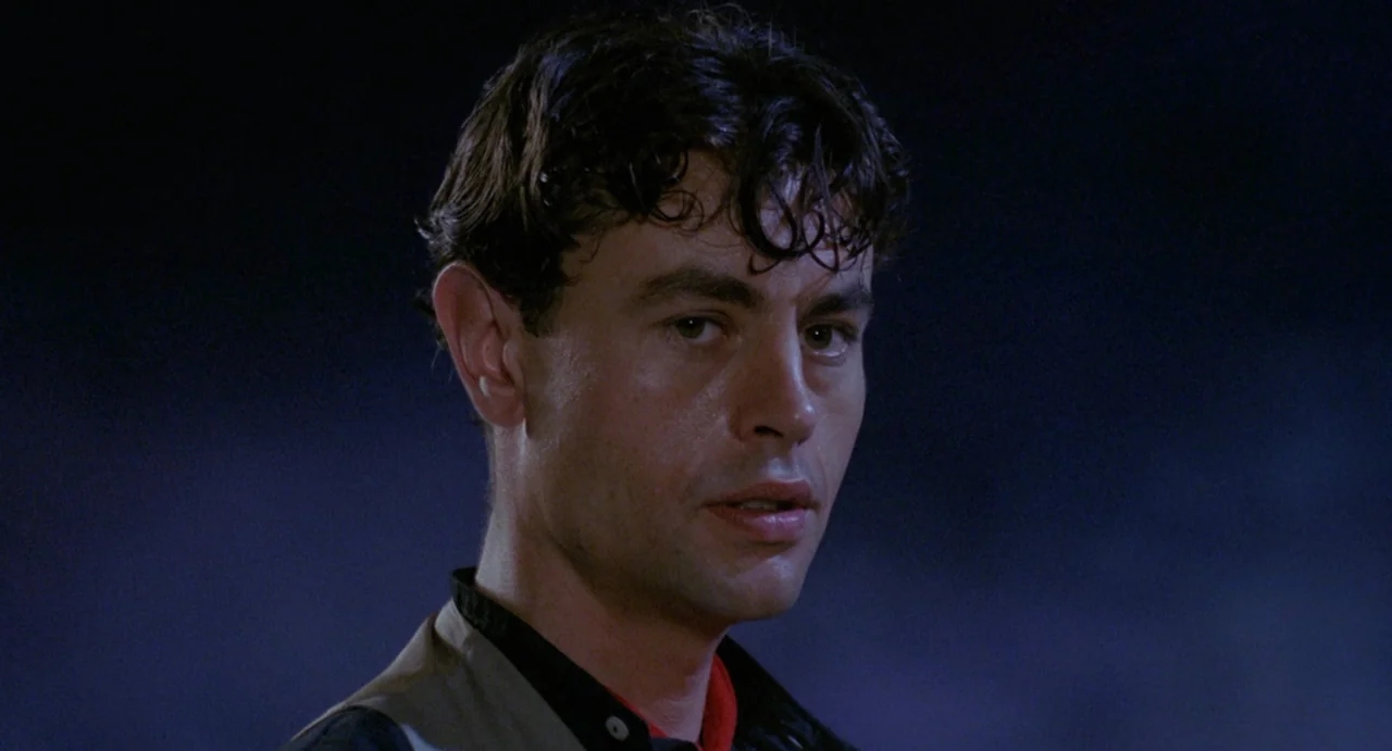 StageFright (1987) movie still: closeup — A man stands against a dark, featureless night background. The subject faces the camera while lit from the…