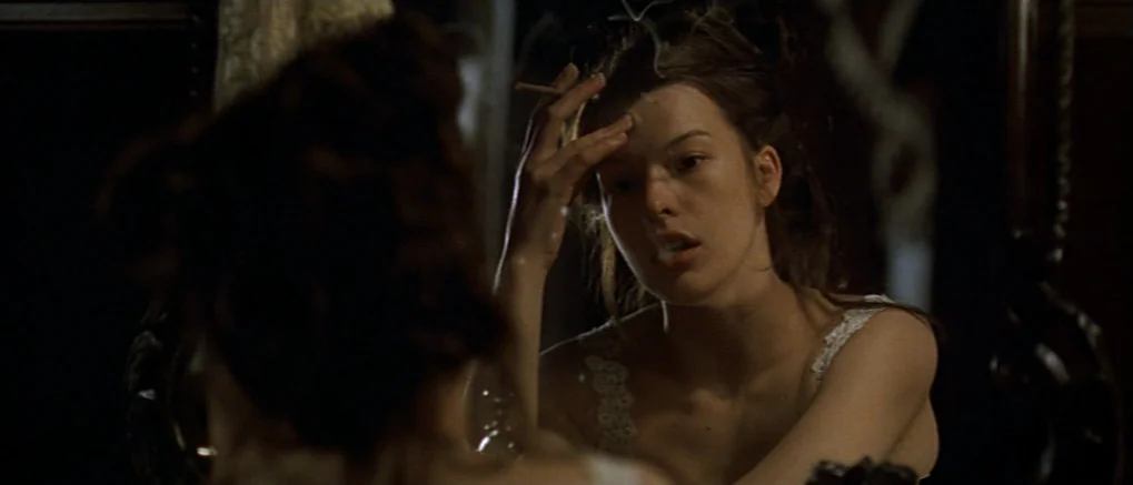The Claim (2000) movie still: closeup — A dimly lit interior space contains a dark wooden vanity mirror with ornate frames. A woman gazes at her own…