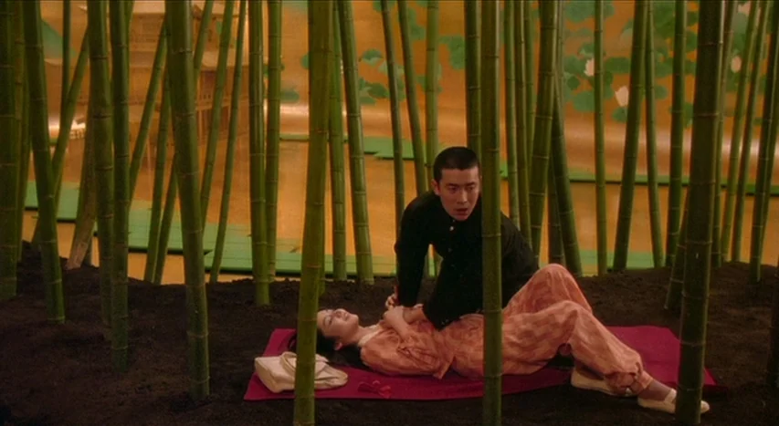 Mishima: A Life in Four Chapters (1985) movie still: medium — An indoor bamboo forest stage set features green stalks emerging from dark soil. A man…