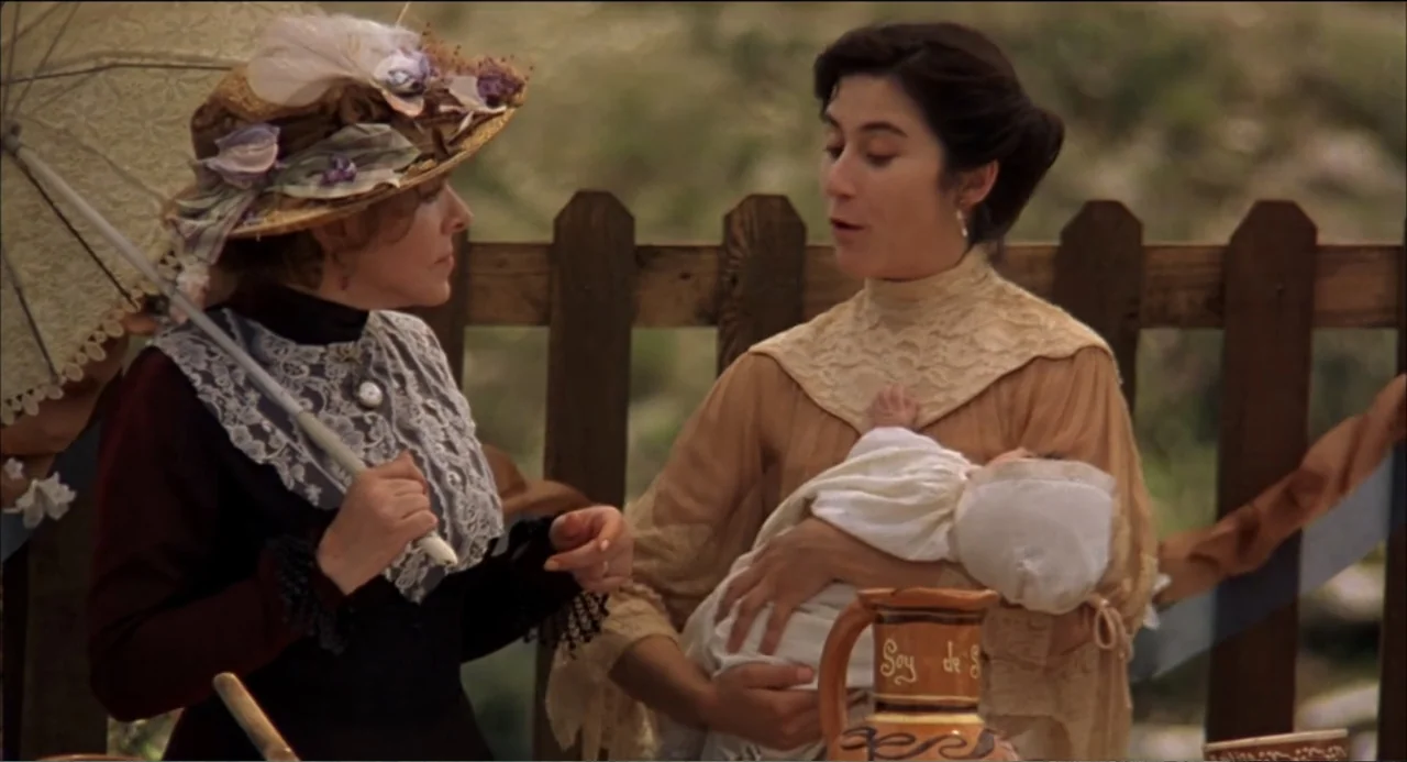 Like Water for Chocolate (1992) movie still: medium — A wooden fence serves as a backdrop for two women in historical attire. One woman carries a…