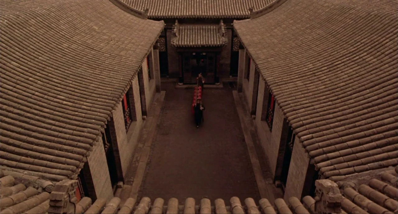 Raise The Red Lantern movie still: wide — A traditional Chinese siheyuan with gray curved roof tiles surrounding a central paved space. A lone…