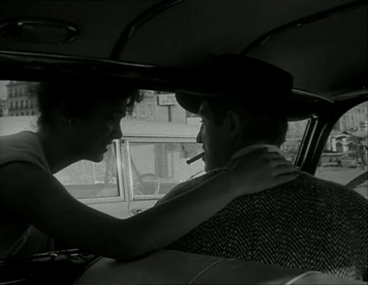 À Bout De Souffle (Breathless) (1960) movie still: medium — A woman leans into the passenger window of a vintage car parked outdoors. She places her…