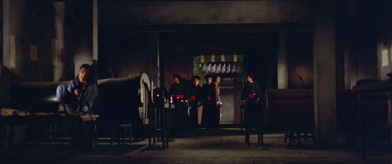 Encounter of the Spooky Kind (1980) movie still: wide — A dark, sparsely furnished interior with concrete walls and hanging scrolls in the…