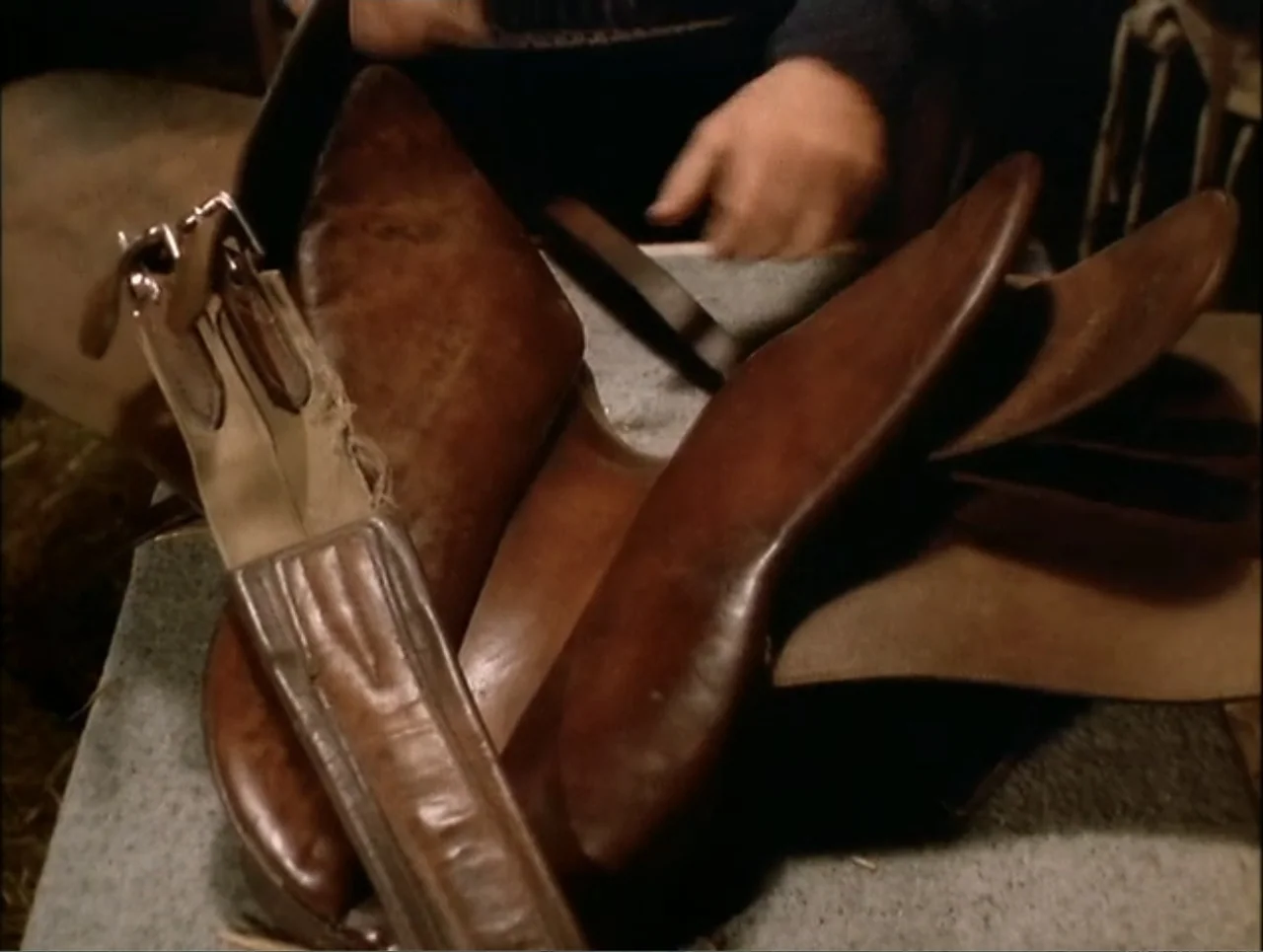 At the Midnight Hour (1995) movie still: closeup — A worn leather horse saddle rests on a workbench in a cluttered space. A person's hands…