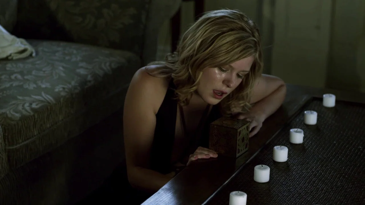 Hellraiser: Revelations movie still: medium — A dimly lit room contains a low coffee table with five small white candles. A young blonde woman leans…