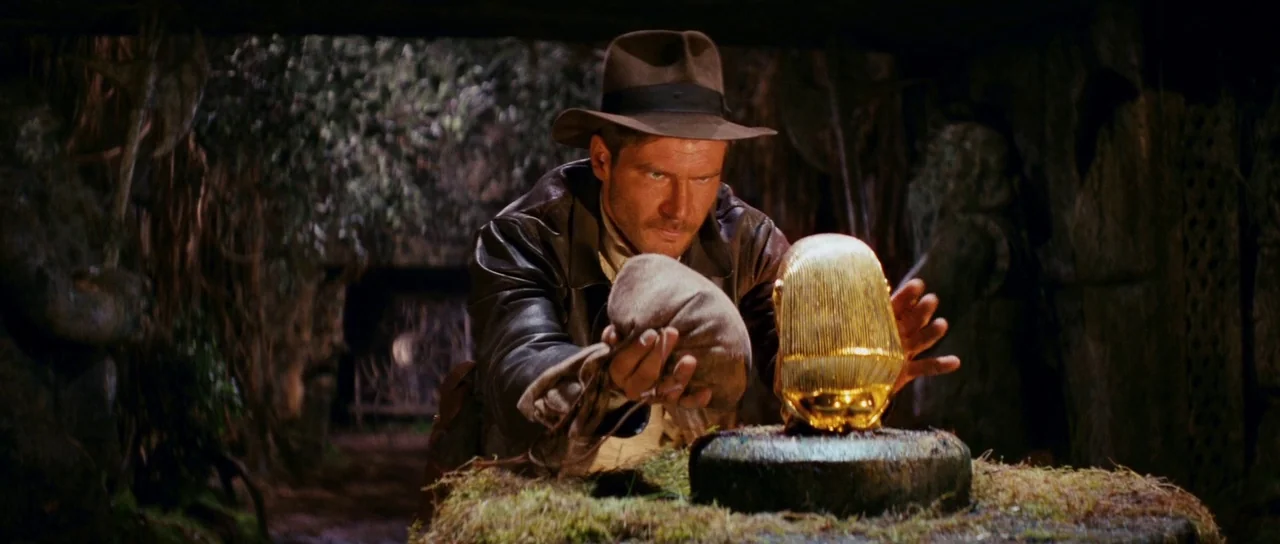 Raiders Of The Lost Ark (1981) movie still: medium — A dark stone chamber contains mossy carvings and walls lined with ancient statues. An…