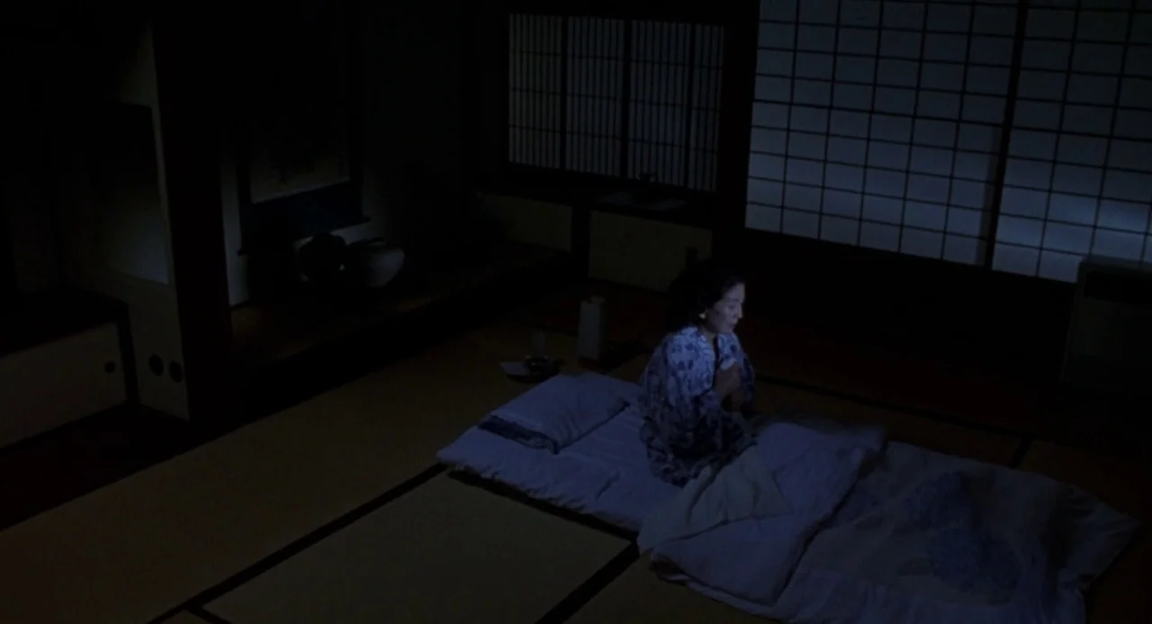Godzilla vs. Destoroyah (1995) movie still: wide — A dark traditional room features tatami mats, shoji screens, and a low platform bed. A woman sits…