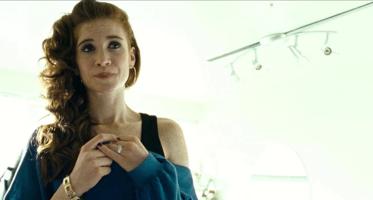 Bronson (2008) movie still: medium — A woman stands in a bright room with overexposed white walls and a ceiling track light. She holds her hands…