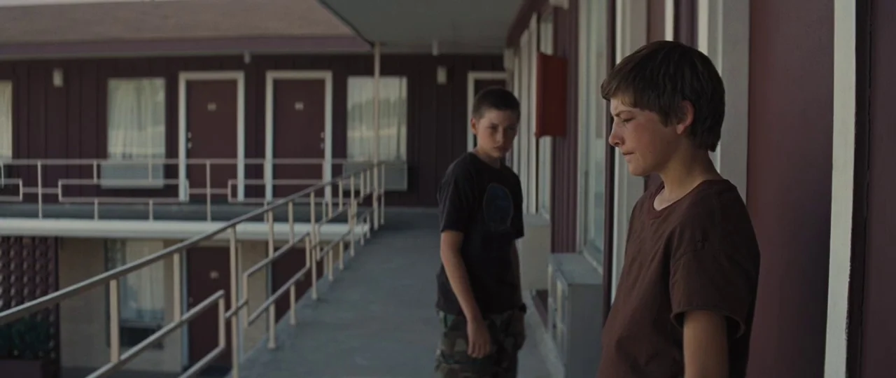 Mud (2012) movie still: medium — A long motel walkway with brown doors and a metal railing lines the building. Two young boys stand along the walkway.