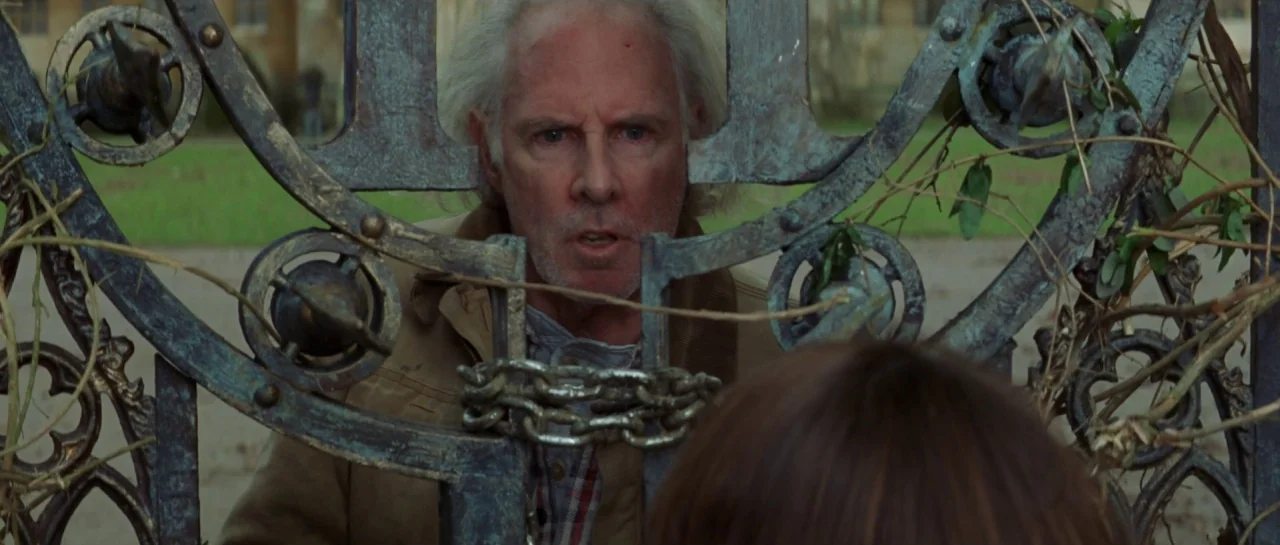The Haunting (1999) movie still: medium — An ornate iron gate with heavy chains separates an older man from a child. The man stands directly behind…