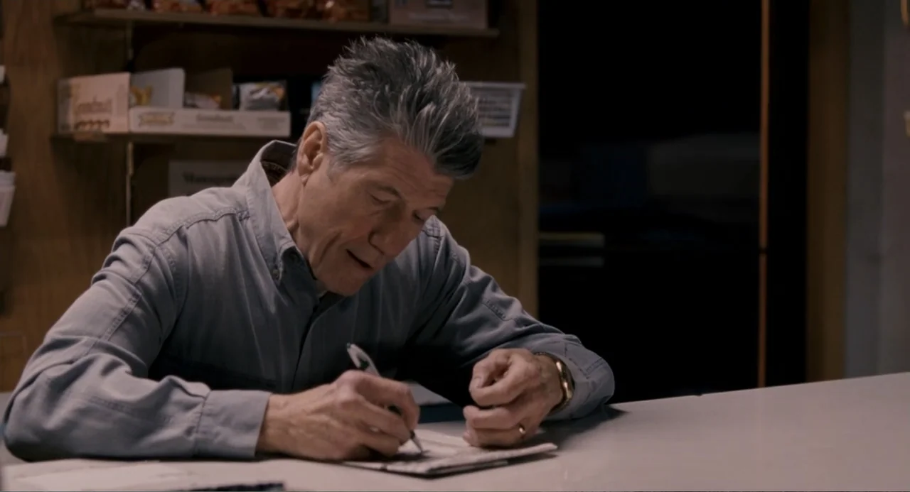 Management (2009) movie still: medium — An interior space features a white counter and shelves stocked with various products. An older man in a blue…