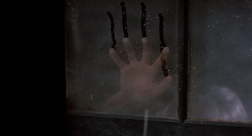 Psycho 2 (1983) movie still: closeup — A dark glass pane is marked with vertical streaks of black liquid. A pale hand presses against the glass from…