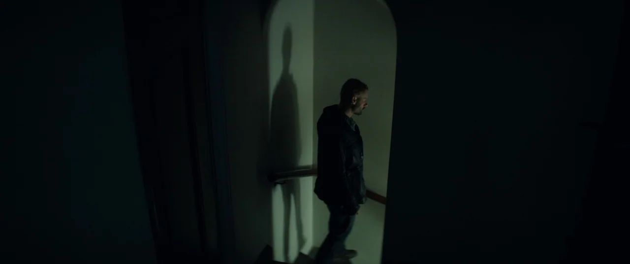 The Empty Man (2020) movie still: fullbody — A dark stairwell with a curved architectural archway illuminated by a dim, directional light. A man…