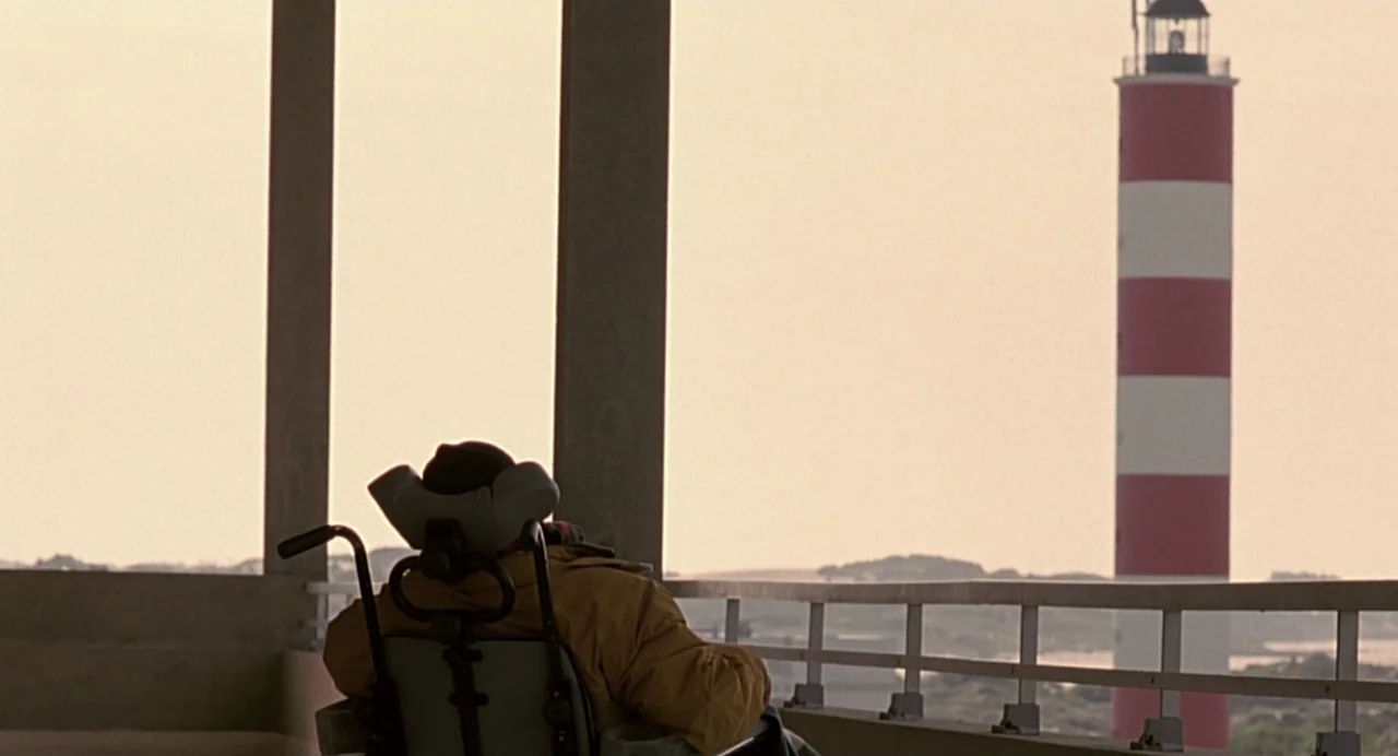 The Diving Bell and the Butterfly (2007) movie still: wide — An outdoor concrete balcony overlooks a coastal landscape with a tall, red-and-white…