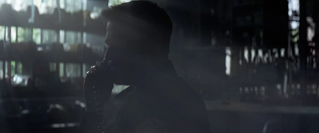Colt 45 (2014) movie still: medium — A dimly lit room with industrial shelving visible in the background against a bright window. A man in uniform…